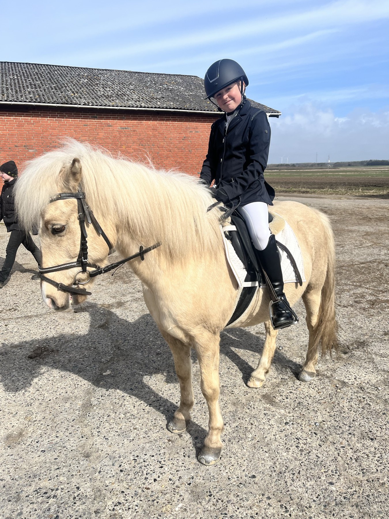 Ellie sidder på Jack — en lys pony — udenfor i solen